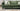 Green fabric corner sofa with wooden legs and striped and plain cushions on a light carpet in a modern living room