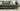 Green fabric Penny 3 seater sofa with striped and white cushions on a light carpet in a modern living room.