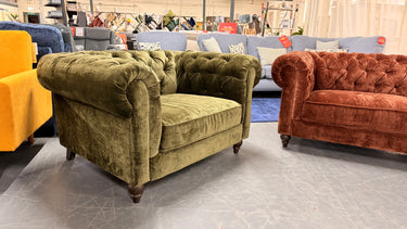 Olive green velvet Chesterfield armchair with rolled arms and deep button tufting in warehouse showroom setting